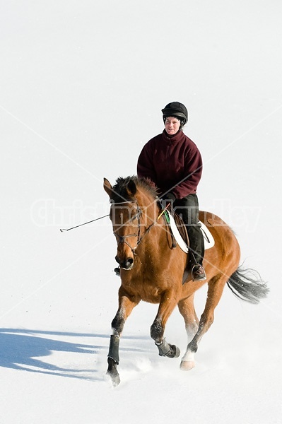 Woman riding bay horse through the deep snow