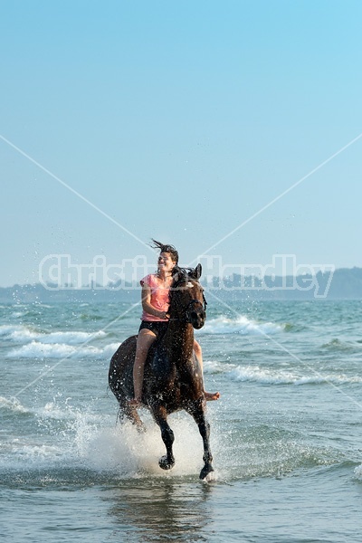 Young woman horseback riding in the surf of Lake Ontario. 