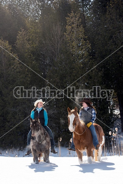 Two young woman riding horses bareback through deep snow