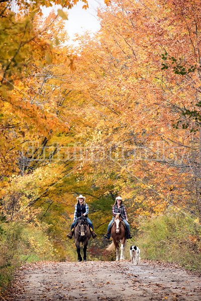 Two young women horseback riding through autumn colored scenery