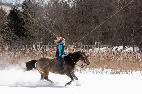 Young woman riding a horse bareback through deep snow