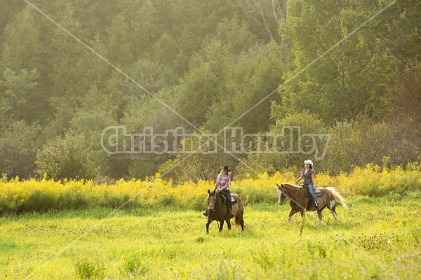 Two young women horseback riding western on a summer evening