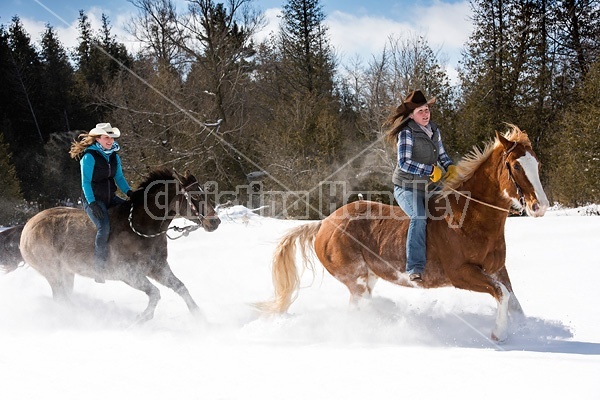 Two young woman riding horses bareback through deep snow