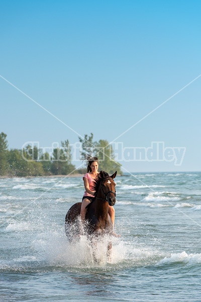 Young woman horseback riding in the surf of Lake Ontario. 